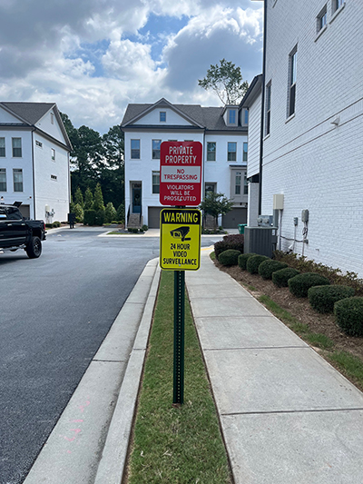 Red private property no trespassing sign with yellow video surveillance warning on a green post in a Georgia townhouse community.
