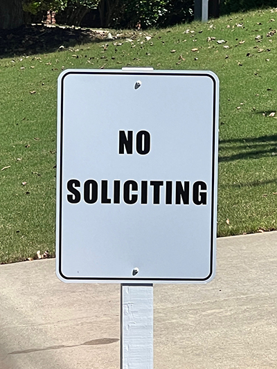White no soliciting sign with bold black lettering mounted on a post in a Georgia subdivision.