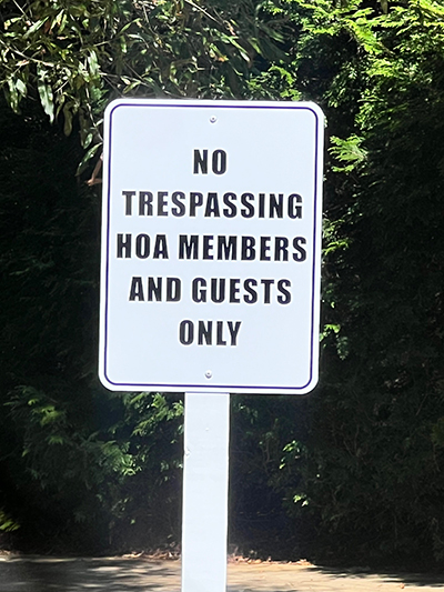 White no trespassing sign stating HOA members and guests only, installed at a Georgia neighborhood entrance.