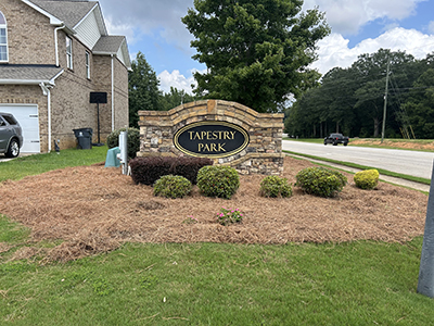 Stone monument sign with black and gold Tapestry Park community name panel at subdivision entrance in Georgia.