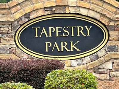 Close-up of Tapestry Park community name sign with gold lettering on black inset within stone monument.