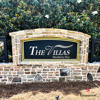 Stone monument entrance sign for The Villas at Blackberry Run featuring a black sign face with gold trim and decorative masonry in Dallas, GA.