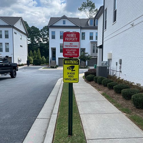 Red private property no trespassing sign with yellow video surveillance warning on a green post in a Georgia townhouse community.